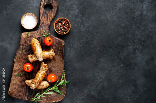 Grilled sausages with spices, tomatoes, rosemary on a stone background with copy space for your text