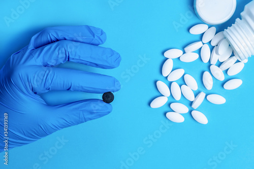 White pills and a black pill in hand with blue glove. Different pills. Medical and different concept of light blue paper background with copy space.