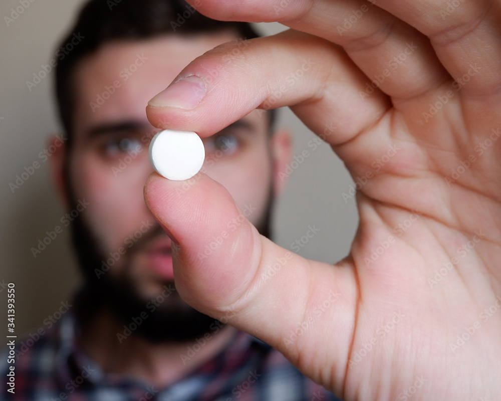 Closeup portrait of a man holding a tablet or capsule with his fingers. A prescription for treatment with a drug A pharmaceutical preparation, a medicine in a container for health. Closeup portrait of a man holding a tablet or capsule with his fingers. A prescription for treatment with a drug A pharmaceutical preparation, a medicine in a container for health.