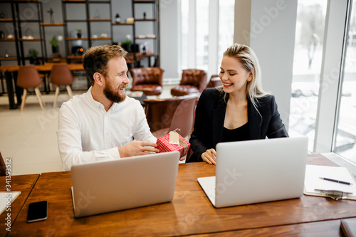 A bearded man Manager sits at the office Desk and gives a gift to his beautiful colleague at work