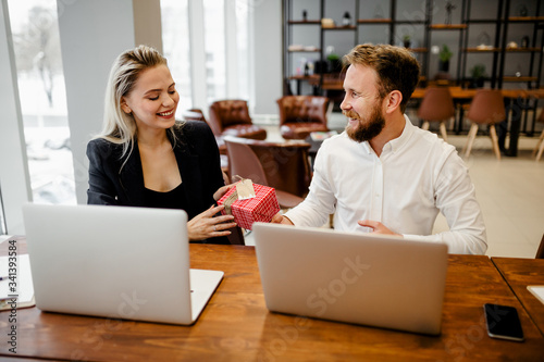 A bearded man Manager sits at the office Desk and gives a gift to his beautiful colleague at work