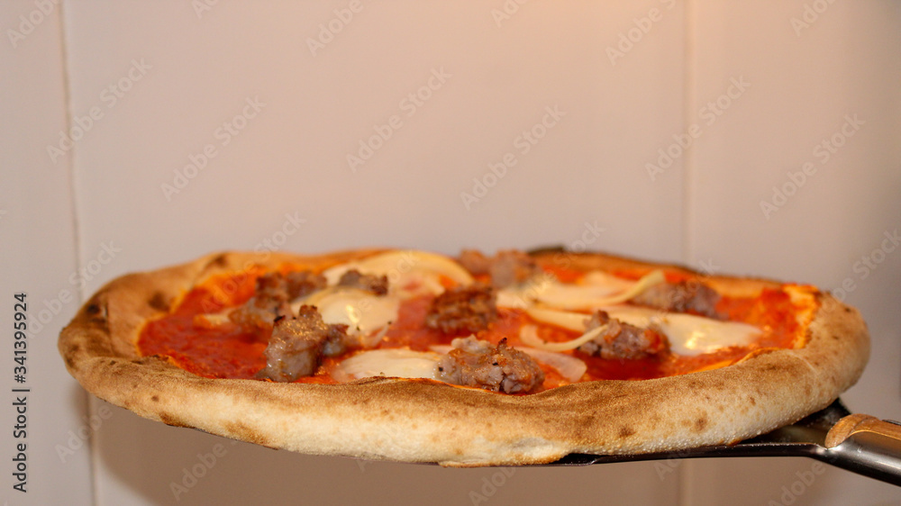 Tasty homemade Italian Pizza with salsiccia on an old wooden paddle straight from a wood fired oven Tasty homemade Italian Pizza with salsiccia on an old wooden paddle straight from a wood fired oven