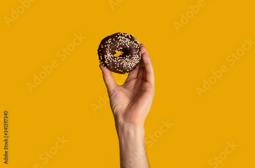 Millennial guy showing yummy chocolate donut on orange background, closeup