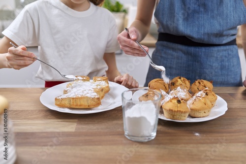 Kids sprinkling baked homemade muffins with white sugar powder