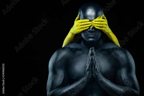 Man with female hands on the body. Bodybuilder athlete with yellow face art and body paint. Colorful portrait of the guy with bodyart.