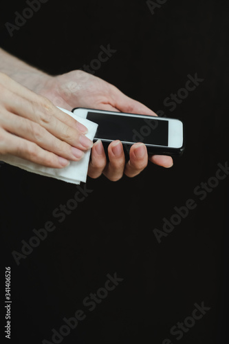 Male hand with a sanitizer spray disinfect the surface of the smartphone on black background. Covid-19 Coronavirus Quarantine Pandemic. Isolation at home. Protect yourself and your loved ones.