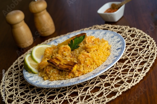 Rice with shrimp, traditional dish of Ecuadorian cuisine, served on wooden table, salt, pepper.