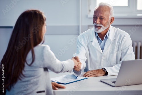 Happy senior doctor handshaking with female patient at doctor's office.