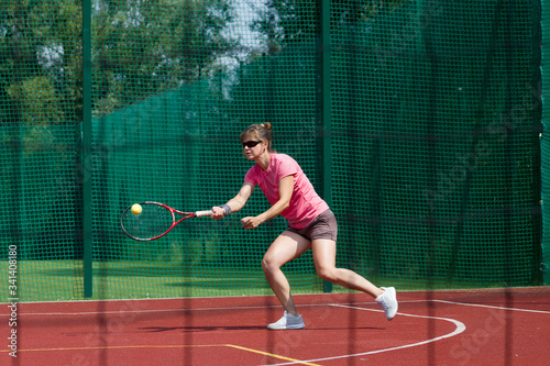 Female tennis player hitting forehand. View through net.