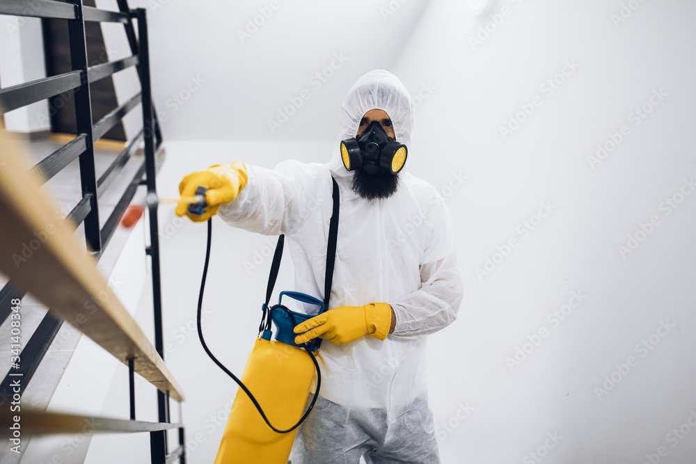 Exterminator in work wear spraying pesticide with sprayer.