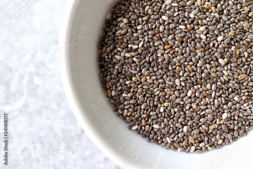 Extreme macro of chia seeds in white bowl on pale gray table. Closeup, horizontal, top view, flat lay.