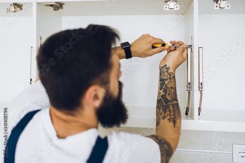 Young bearded handyman working in the kitchen. Renovation.