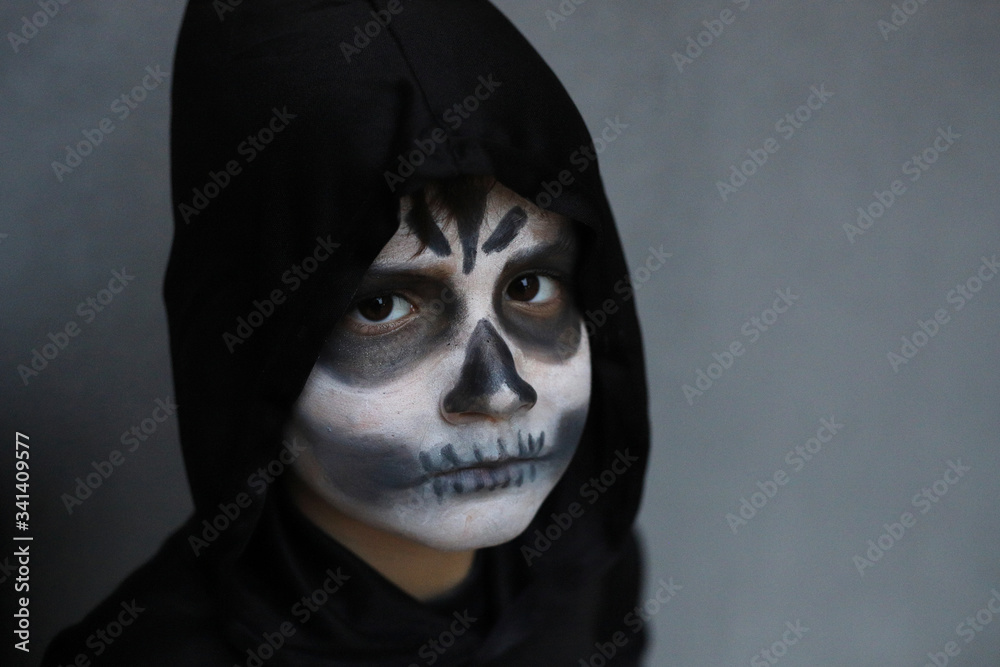 niño con disfraz de muerte con la cara pintada como una calavera yla  capucha negra puesta Stock Photo | Adobe Stock