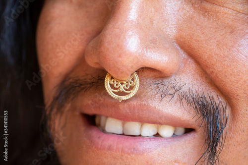 Portrait of young hispanic man with long hair wearing a metal septum piercing at his nose
