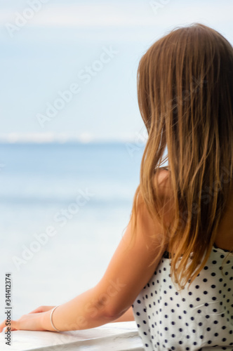 a girl with blond hair stands by the railing and looks out at the sea