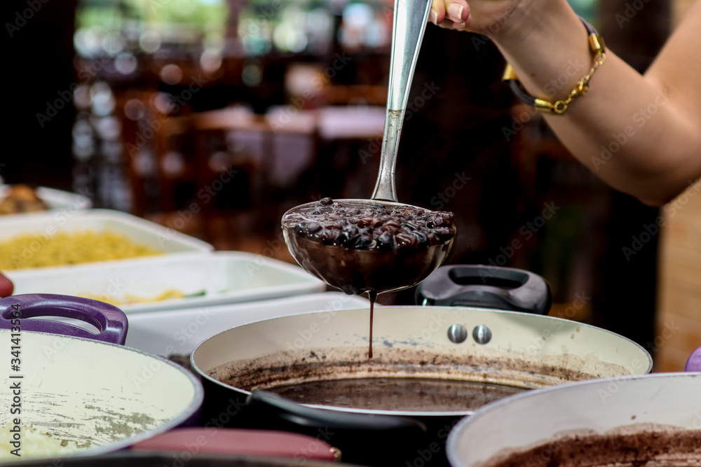 Fotografie hand holding spoon with brazilian feijoada.
