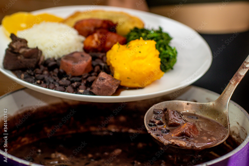 hand holding spoon with brazilian feijoada to serve on plate hand holding spoon with brazilian feijoada to serve on plate