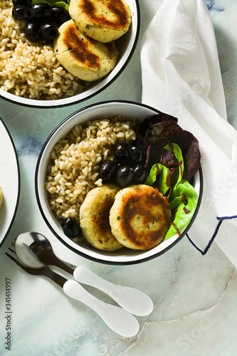 A simple vegan lunch or dinner for a family of two adults and a child. brown rice with soy okara and potato patties with fresh salad and olives on a marble table photo