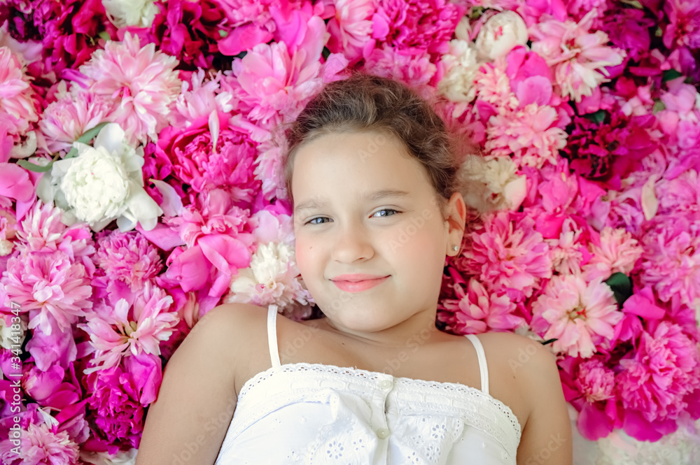 Greeting card mother's day. Cheerful smiling girl on a background with pink peonies. Smiling girl on pink background of peonies. Pink floral background of fresh pink peony flowers buds. Greeting card mother's day. Cheerful smiling girl on a background with pink peonies. Smiling girl on pink background of peonies. Pink floral background of fresh pink peony flowers buds.