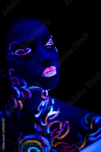 fantastic unusual shot of young caucasian woman with fluorescent make-up glowing in ultra-violet light. body art on attractive woman, unusual colorful design
