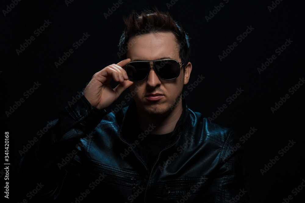 Young sexy stylish guy with glasses in a black leather jacket on a black background Young sexy stylish guy with glasses in a black leather jacket on a black background