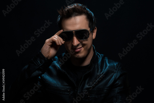 Young sexy stylish guy with glasses in a black leather jacket on a black background