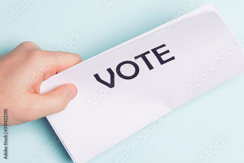 Paper with vote inscription, male hand on a blue background
