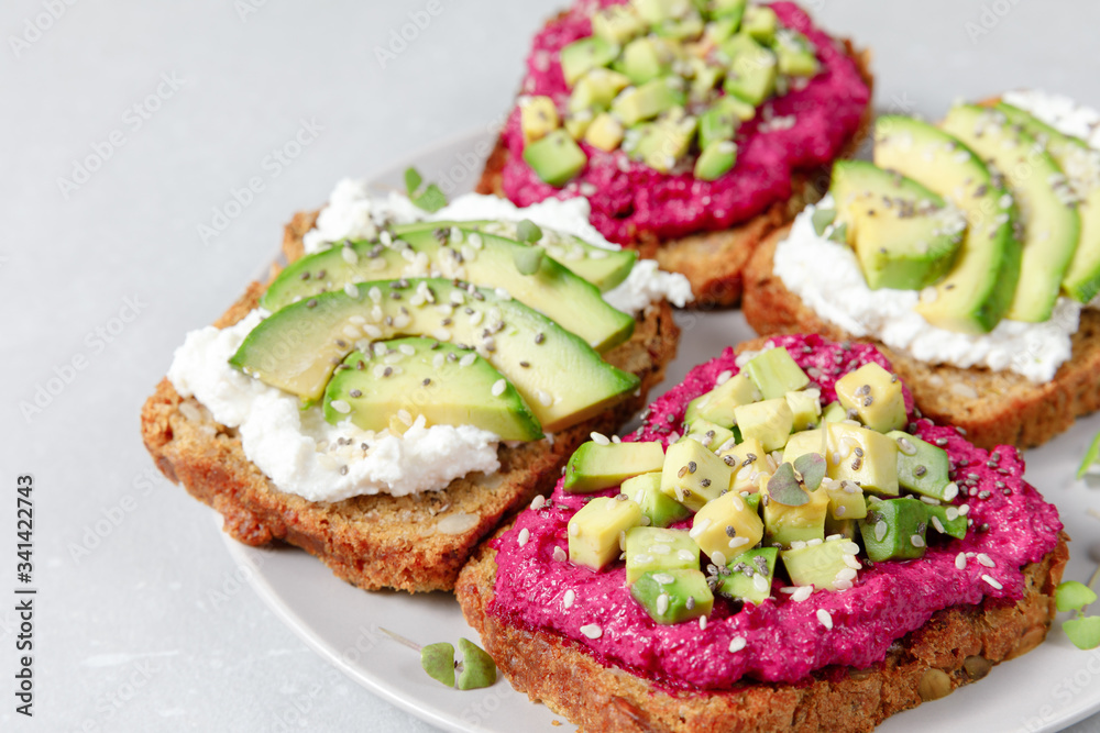 Variation of healthy sandwiches with avocado beetroot cream cheese and whole wheat rye bread on a plate on grey background. Delicious snacks and toast. Food composition. Close up, top view Variation of healthy sandwiches with avocado beetroot cream cheese and whole wheat rye bread on a plate on grey background. Delicious snacks and toast. Food composition. Close up, top view