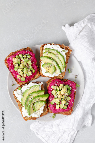 Variation of healthy sandwiches with avocado beetroot cream cheese and whole wheat rye bread on a plate on grey background. Delicious snacks and toast. Food composition. Top view