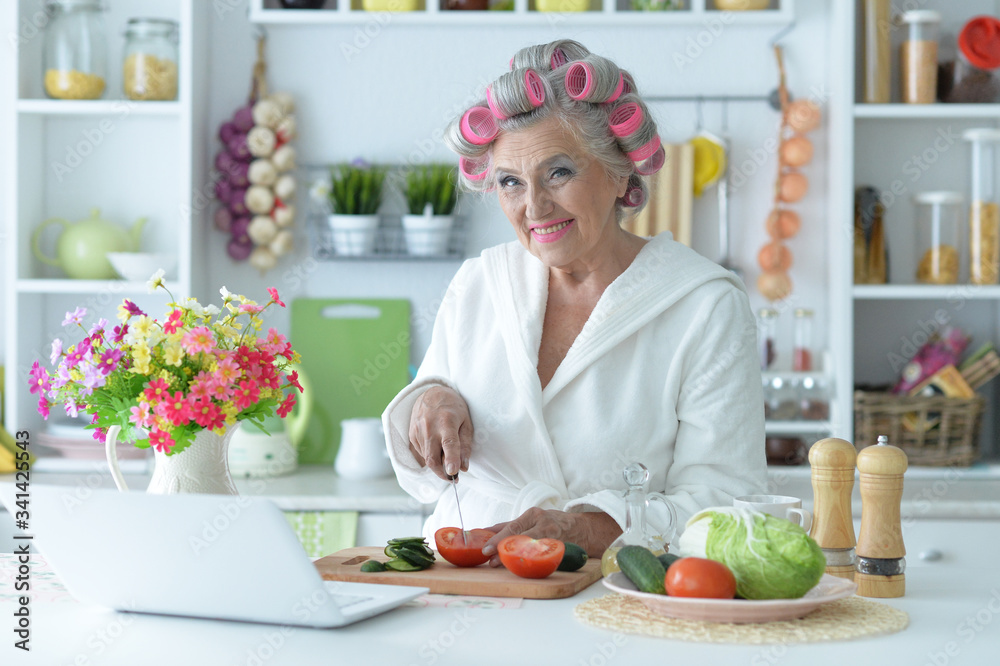 Senior woman in hair rollers cutting vegetables on kitchen table Senior woman in hair rollers cutting vegetables on kitchen table