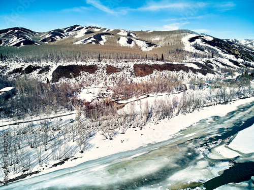 Panoramic aerial view: beautiful spring landscape: the Ulba river in Kazakhstan wakes up from winter sleep - ice drift - snow and ice are melting in the mountains, the bright sun is shining photo