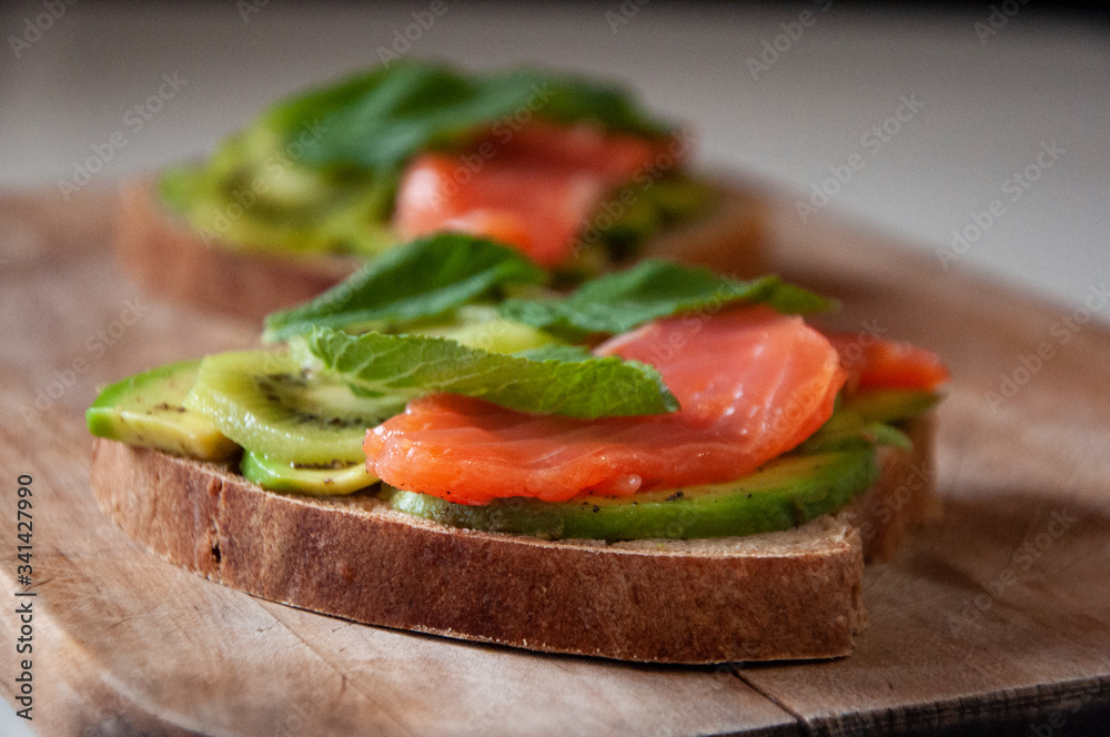 Healthy sandwich for breakfast made with home baked bread, salted salmon, avocado, kiwi and mint leaves. Healthy sandwich for breakfast made with home baked bread, salted salmon, avocado, kiwi and mint leaves.