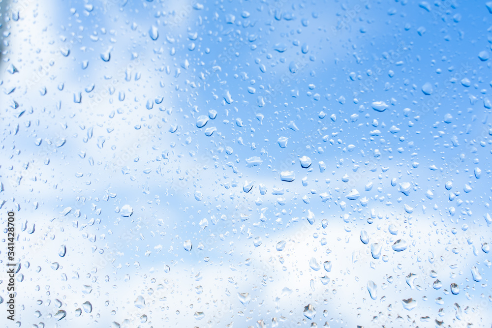 Raindrops on window glass against blue sky with white clouds