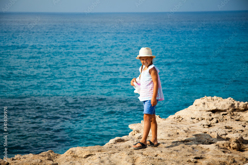 Little girl with toy standing on the rock with blue sea on background