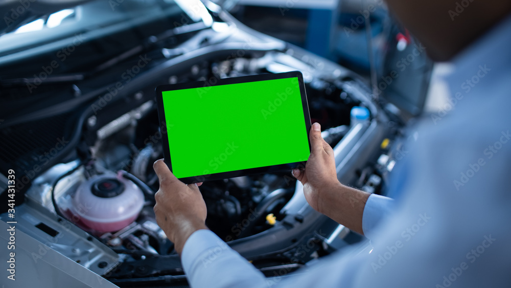 Car Service Manager or Mechanic Uses a Tablet Computer with a Green Screen Mock Up that is Pointed at an Enginer Bay. Specialist Inspecting the Vehicle in Order to Find Broken Components In the Engine Car Service Manager or Mechanic Uses a Tablet Computer with a Green Screen Mock Up that is Pointed at an Enginer Bay. Specialist Inspecting the Vehicle in Order to Find Broken Components In the Engine