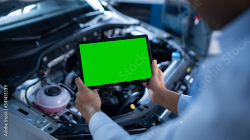 Car Service Manager or Mechanic Uses a Tablet Computer with a Green Screen Mock Up that is Pointed at an Enginer Bay. Specialist Inspecting the Vehicle in Order to Find Broken Components In the Engine