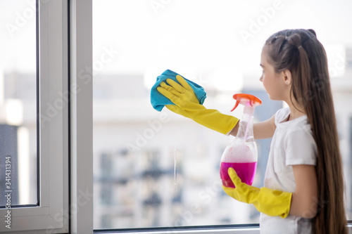 Long-haired girl washing a window with a napkin.
