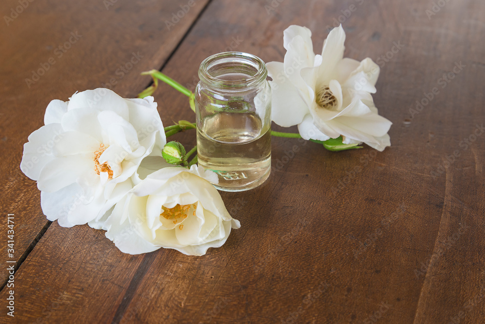 Rose essential oil concept. Vial with essential rose oil and white rose flowers on vintage wooden background Rose essential oil concept. Vial with essential rose oil and white rose flowers on vintage wooden background