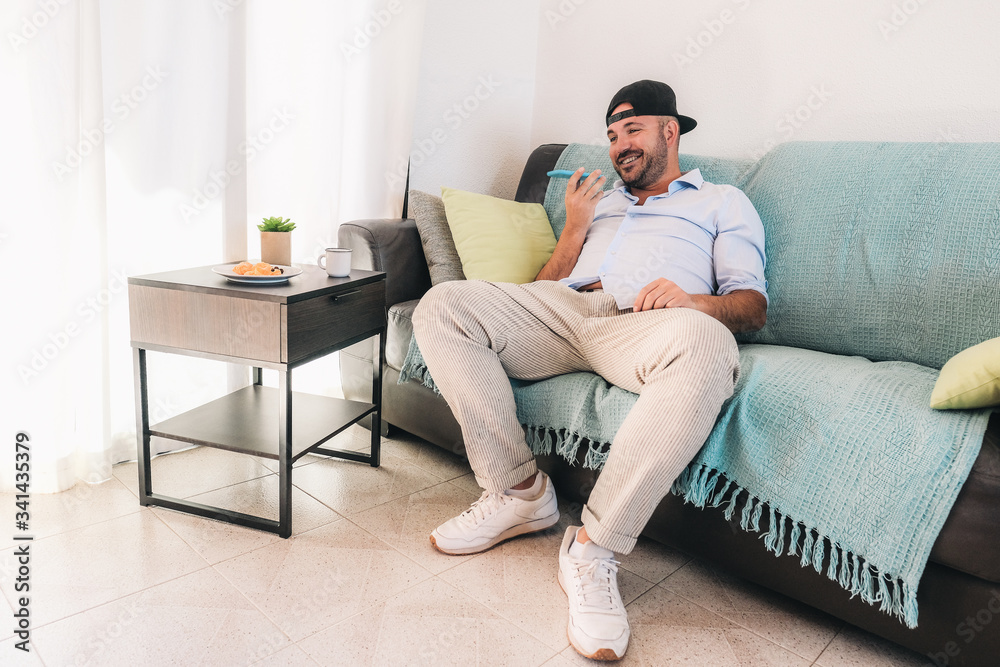 Man holding smartphone near mouth, using virtual assistant service - Smiling young man recording voice message in messenger on mobile phone - isolated at home because of the corona crisis Man holding smartphone near mouth, using virtual assistant service - Smiling young man recording voice message in messenger on mobile phone - isolated at home because of the corona crisis