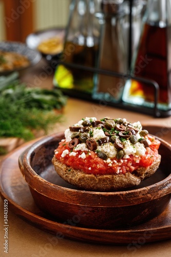 Authehntic greek cuisine fried tomato fritters with greek feta cheese, fresh herbs, oregano, and olives. Presentable appetizer plating on wooden bowl in casual dine in table background.