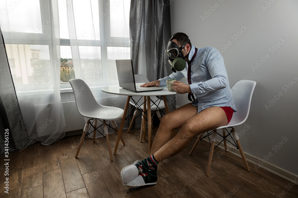 The Manager works at home in quarantine during the pandemic. Protection from the virus. Pandemic covid 19. Works on a laptop at home. Business during self-isolation. Remote work. A man in a gas mask. The Manager works at home in quarantine during the pandemic. Protection from the virus. Pandemic covid 19. Works on a laptop at home. Business during self-isolation. Remote work. A man in a gas mask.