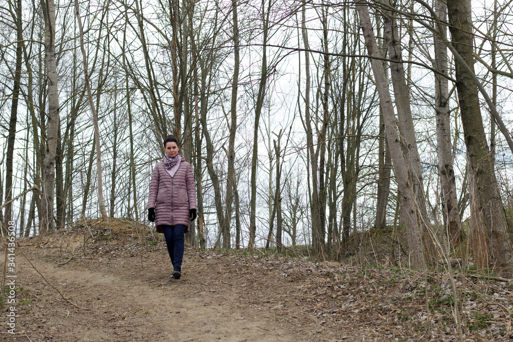 A girl walks through the spring park. Dressed in a spring jacket, a scarf around her neck. Around the blossoming greens on the trees. A girl walks through the spring park. Dressed in a spring jacket, a scarf around her neck. Around the blossoming greens on the trees.