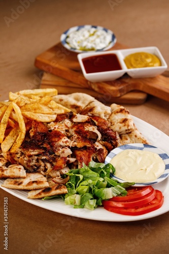 Chicken kontosouvli with pita bread, potato fries, garlic cream and vegetable on the side. Authentic greek cuisine main course plating photography perfect for menu book concept.