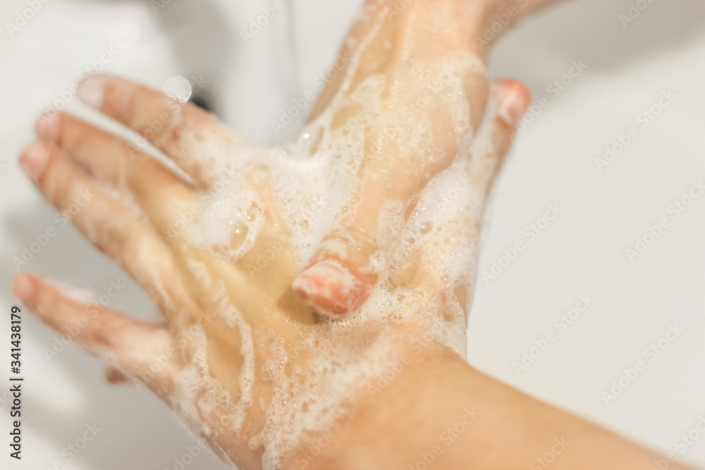 Fototapeta premium Rubbing big thumb, Washing hands with antibacterial soap in proper technique on background of flowing water in white bathroom. Prevention coronavirus. Cleaning and disinfecting