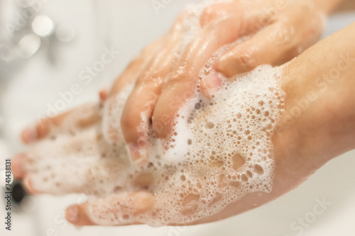 Washing hands. Hands washing with antibacterial soap in proper technique on background of flowing water in white bathroom. Prevention coronavirus. Cleaning and disinfecting hands