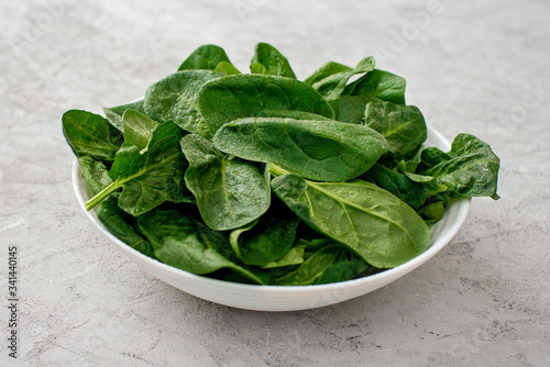 Clean food concept. Leaves of fresh organic spinach greens in a plate on a light background. Healthy detox spring-summer diet. Vegan Raw Food.