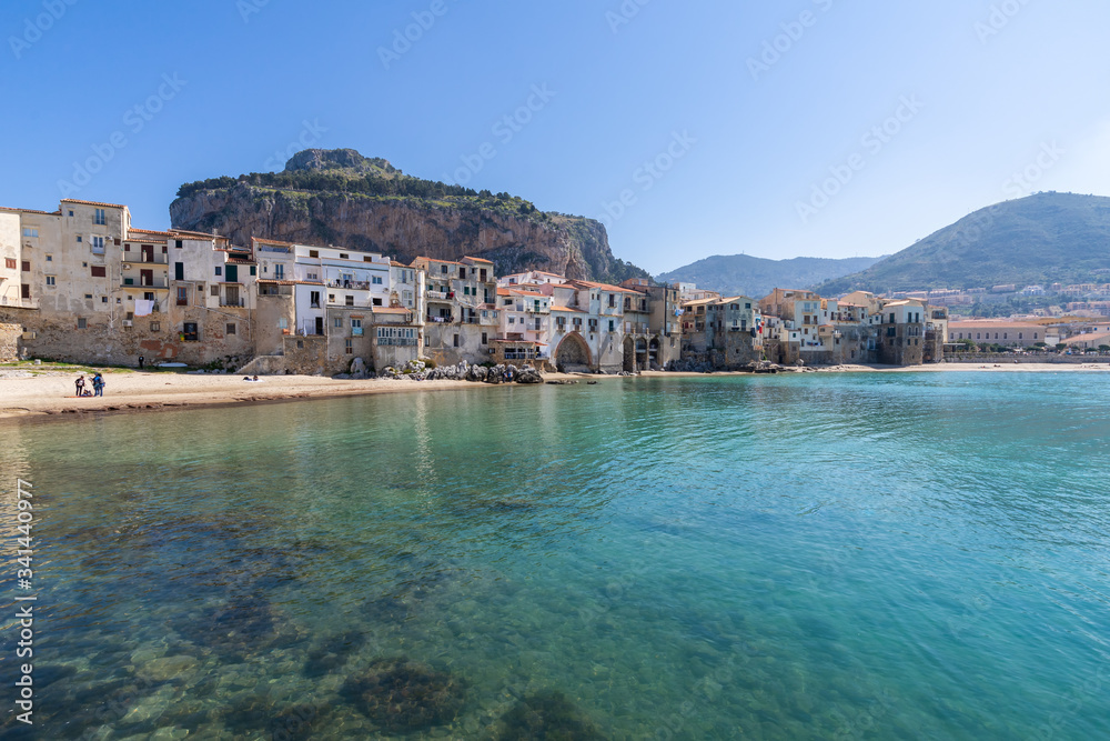 Idyllic view of turquoise sea and houses with Rocca di Cefalu rocky mountain in the background seen from historical old port of Cefalu, Sicily, Italy.