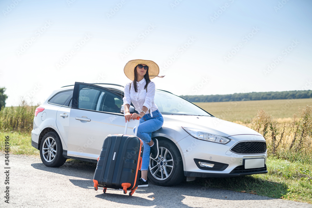 Pretty girl with suitcase standing near car and wiat for her dreaming trip. - obrazy, fototapety, plakaty 