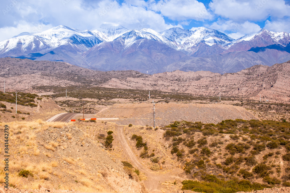 Montanhas com gelo em Mendoza Argentina em ambiente seco e arenoso com uma estrada asfaltada.