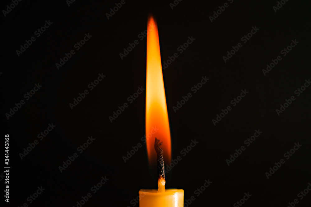 Close-up of a yellow candle illuminated in a black background. Close-up of a yellow candle illuminated in a black background.
